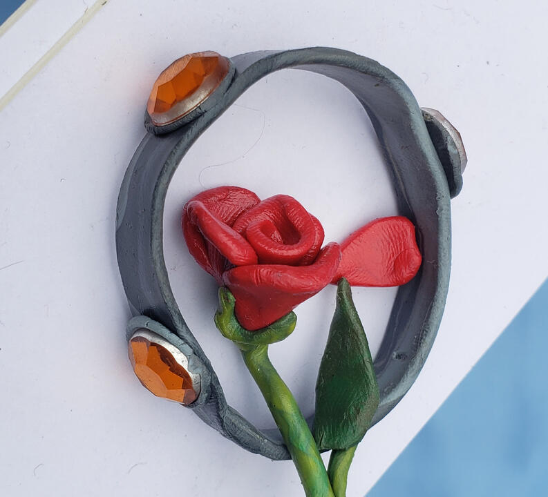 Plasticine illustration of a crown with 3 orange jewels, and a rose with one petal fallen